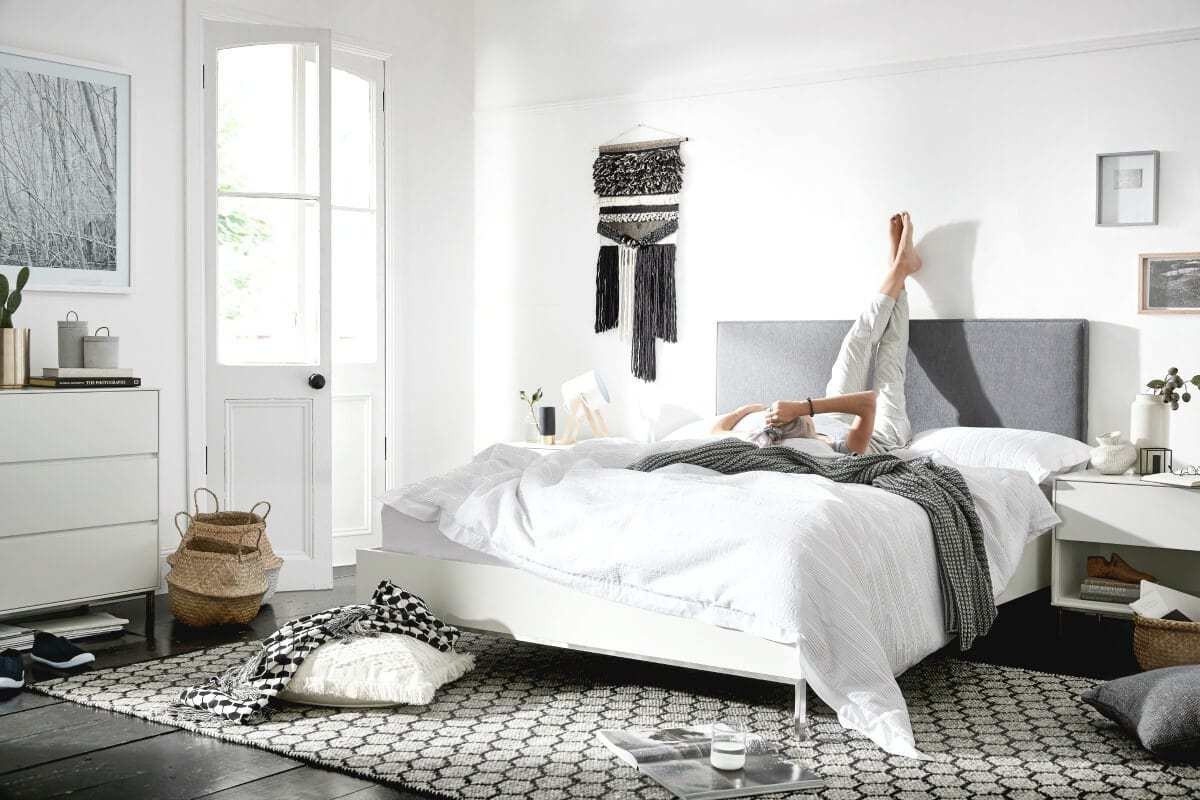 black and white bedroom with grey upholstered headboard macrame wall hanger and belly baskets