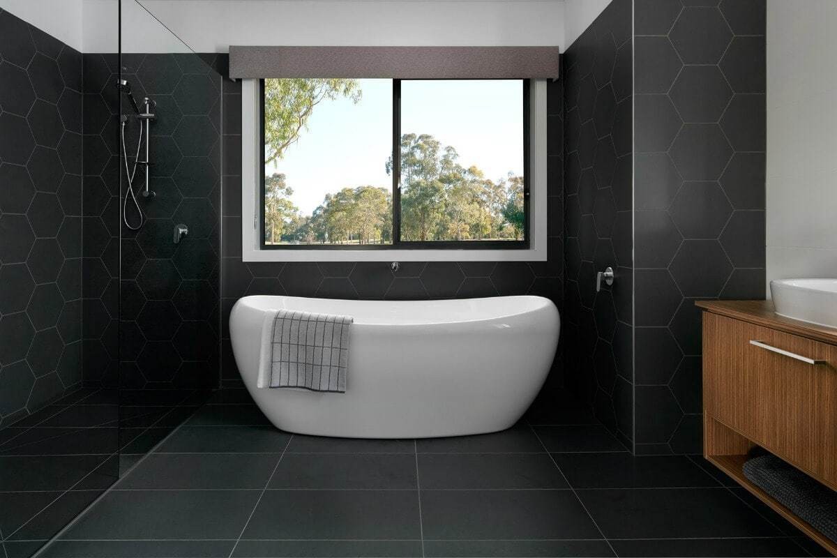 black bathroom hexagonal black wall tiles freestanding bath with view from metricon