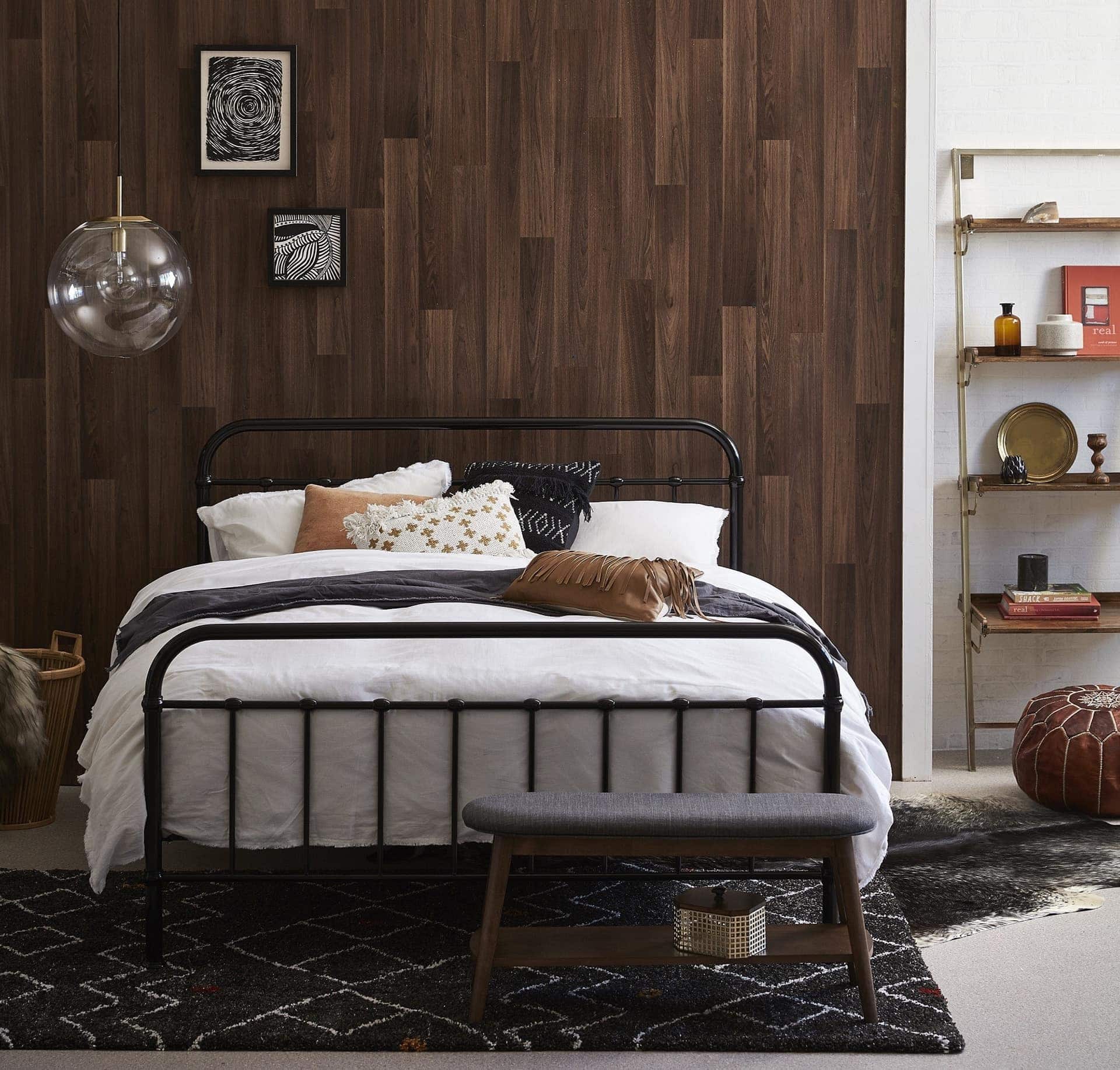 black metal bed frame in bedroom with brown timber wall panels and black diamond rug