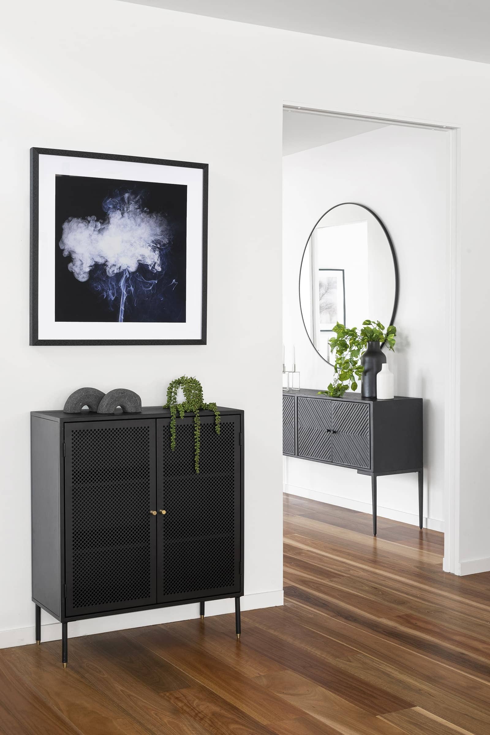 black metal storage unit and black globewest side table in entryway with fake plants