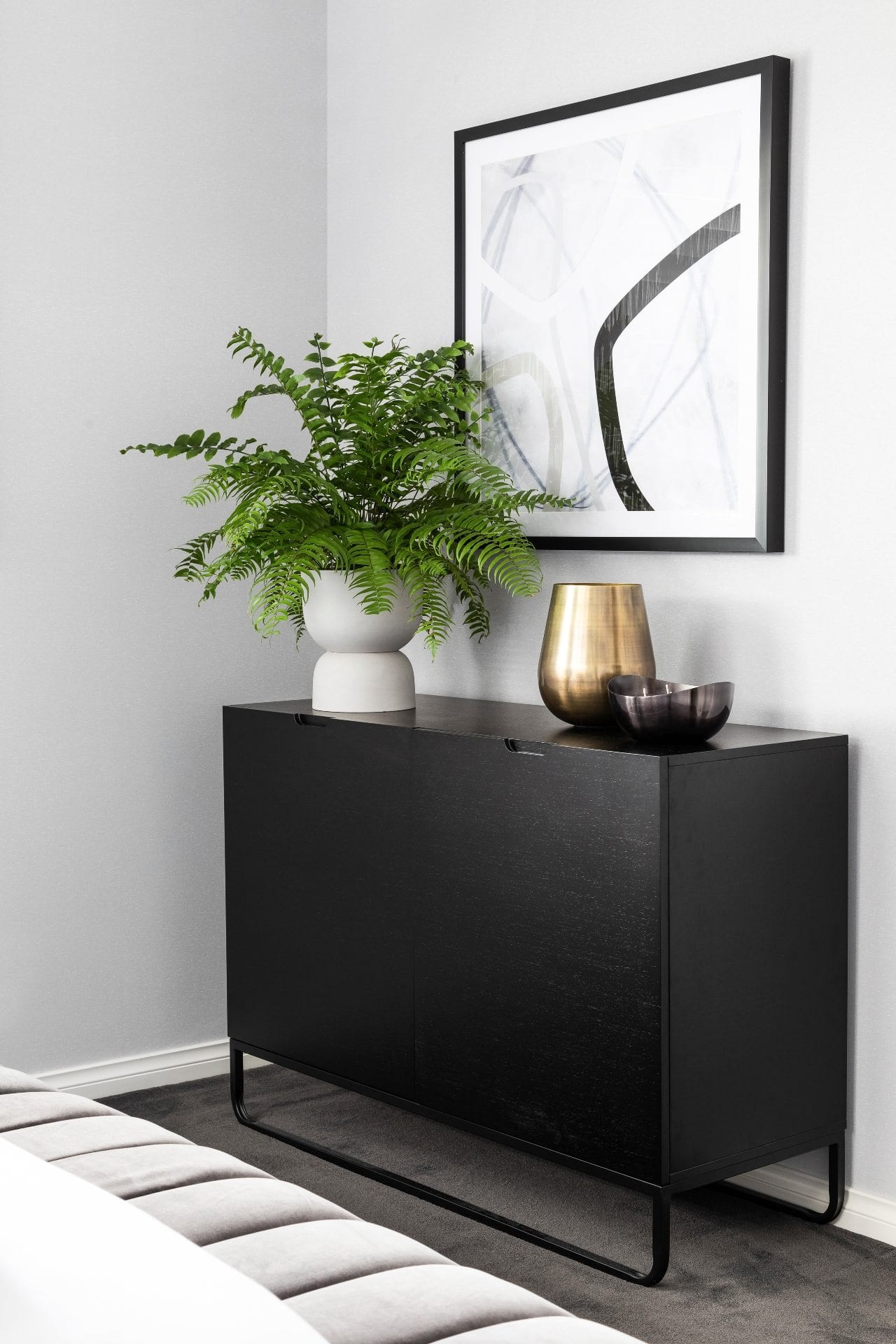 black sideboard with metal legs boston fern indoor plant and black and white abstract art in bedroom