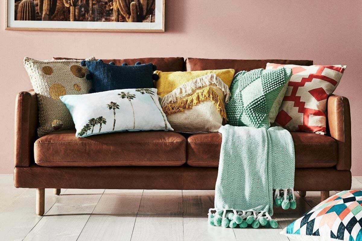 brown leather sofa from freedom with lots of cushions and a turquoise throw with pom poms