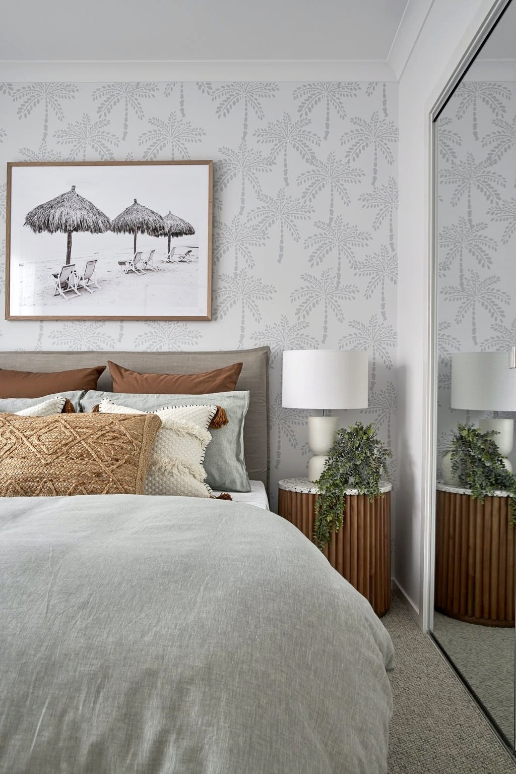 coastal bedroom with palm tree wallpaper and round timber bedside table with marble top