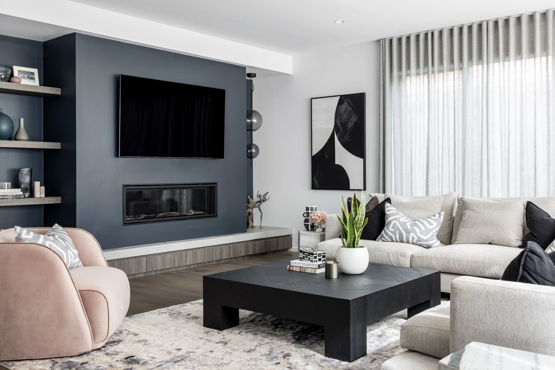 contemporary luxe living room with grey sectional sofa soft pink armchair and dark blue grey feature wall fireplace