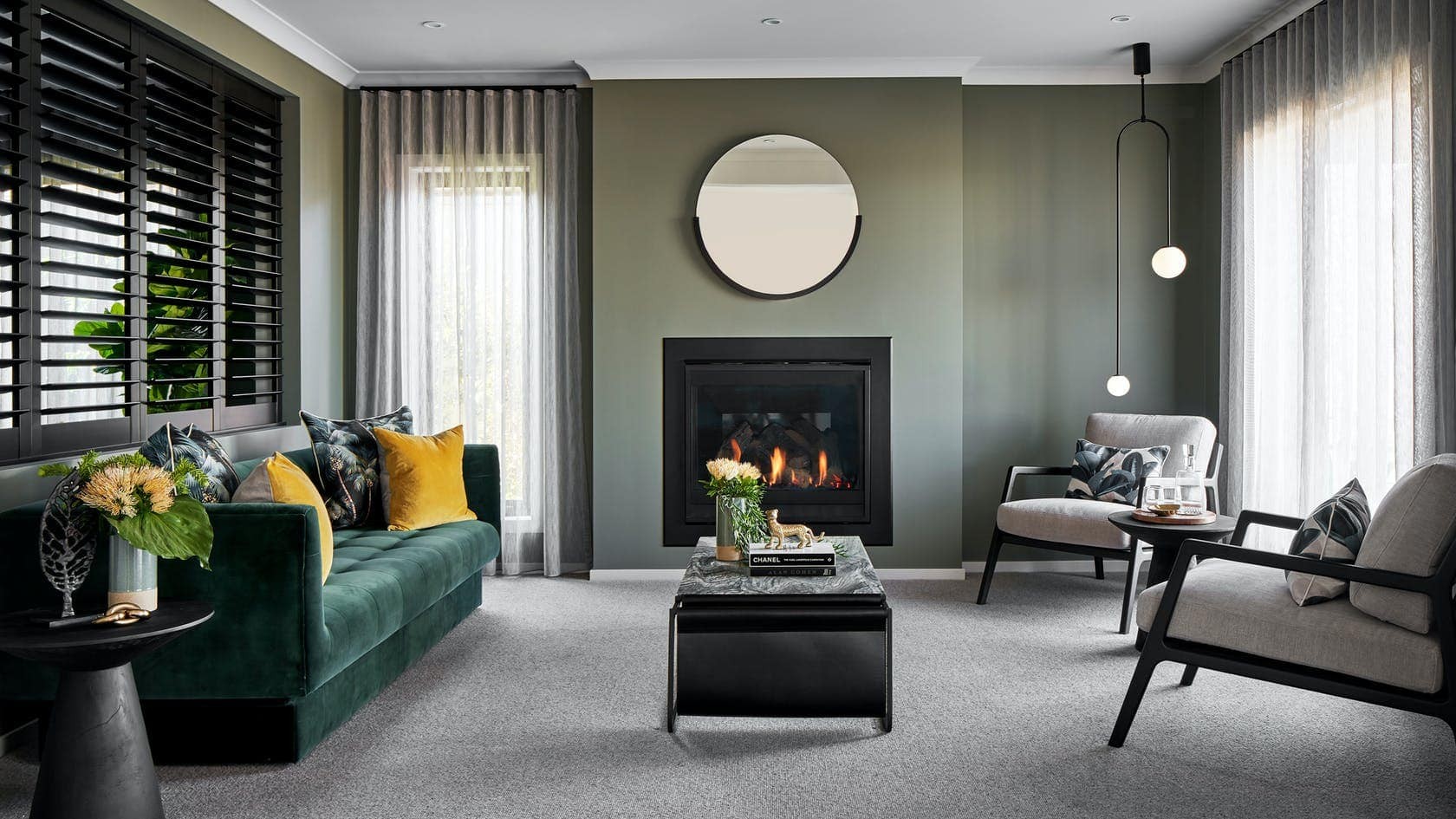 formal living room styling with dark green walls fireplace with round mirror above and velvet green sofa