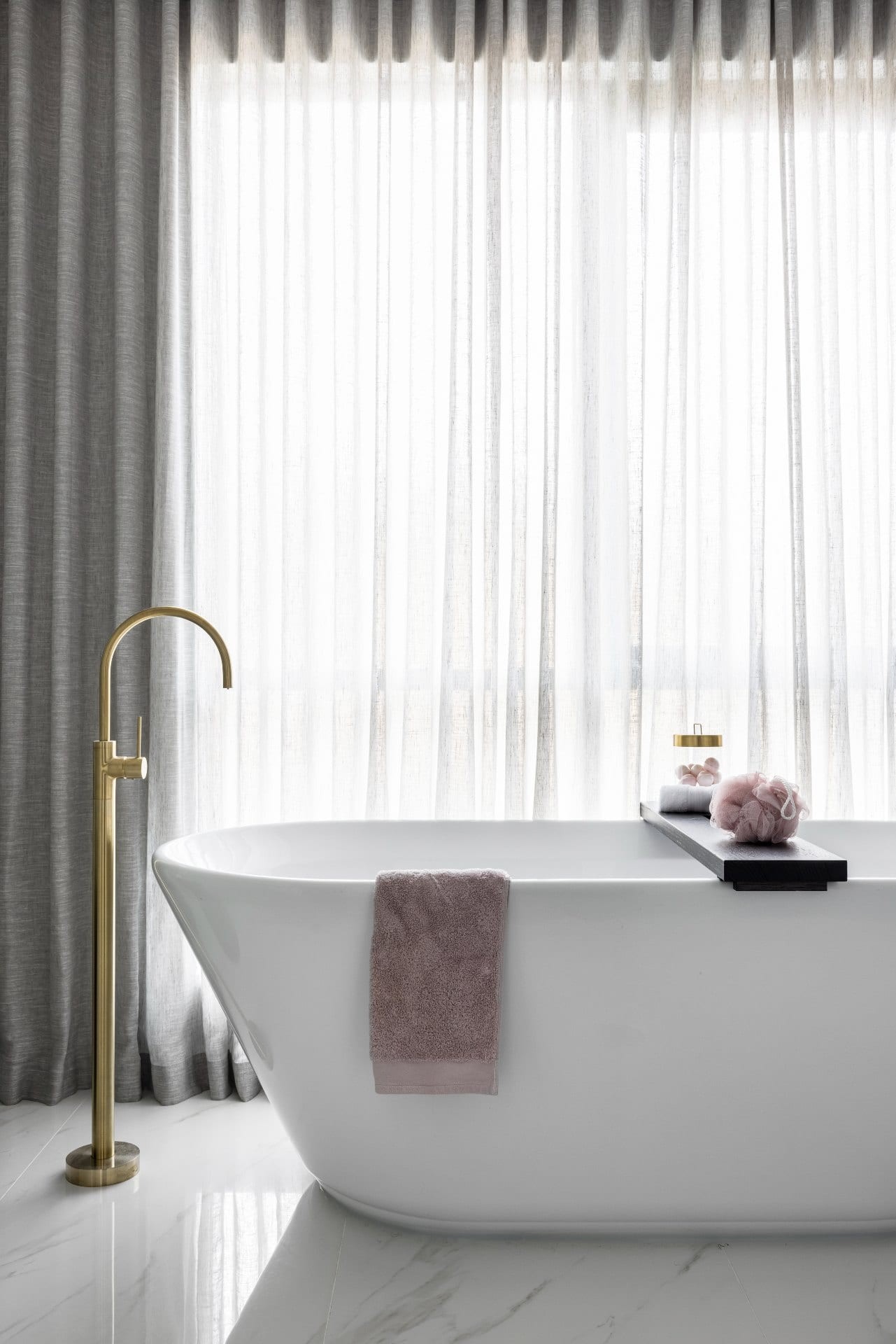 freestanding bath tub with brass floor tap and soft grey sheer curtains