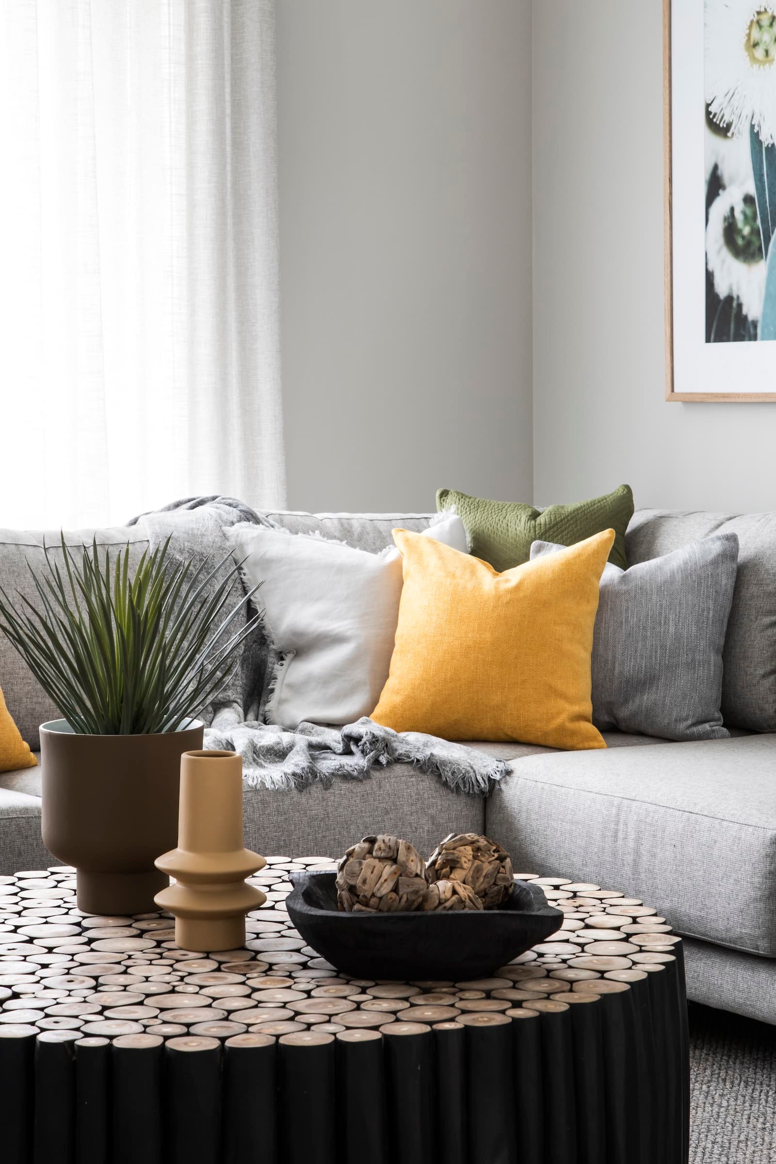green and yellow cushions on grey sectional sofa with round black log coffee table