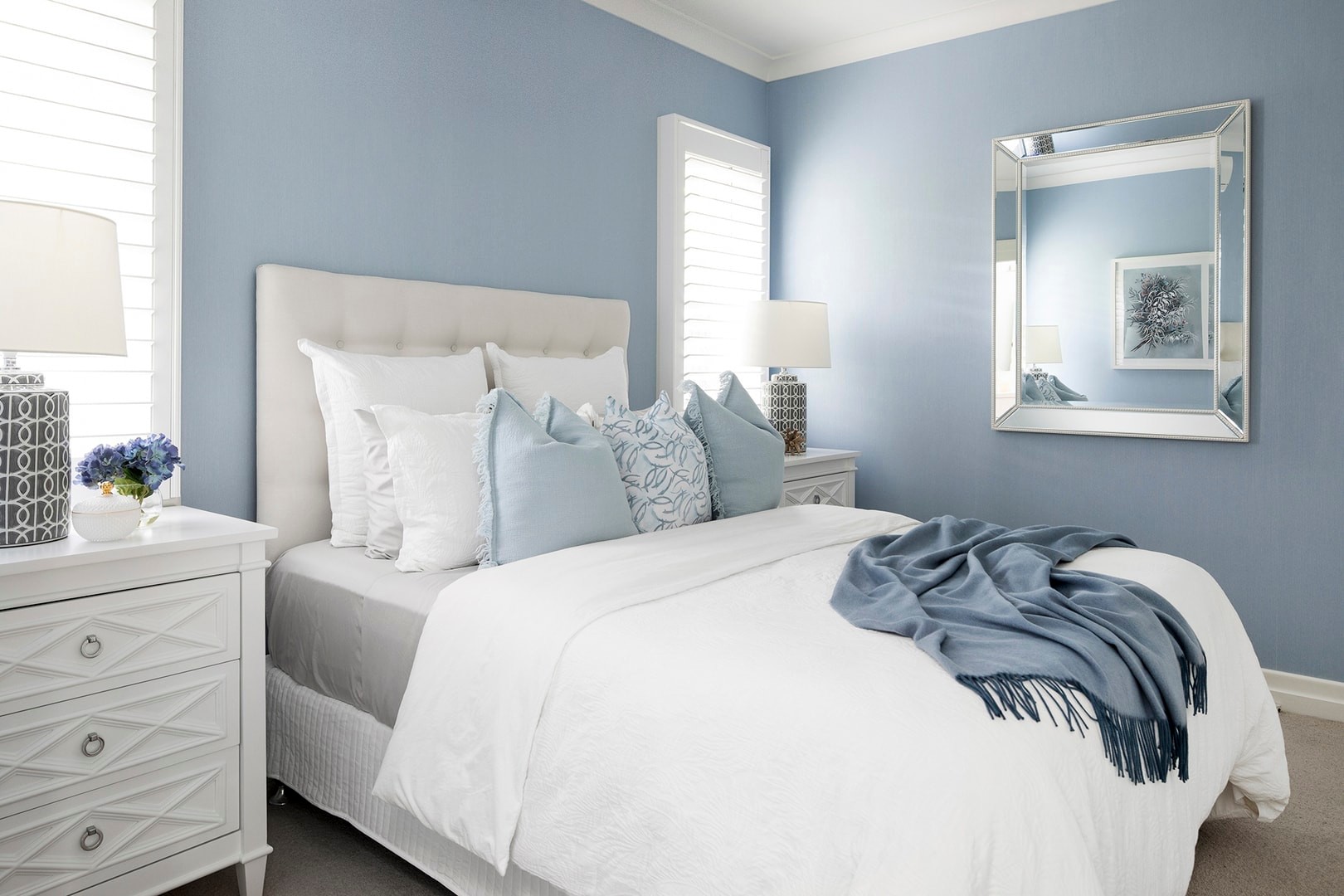 hamptons bedroom with light blue walls cream upholstered headboard and white hamptons bedside tables