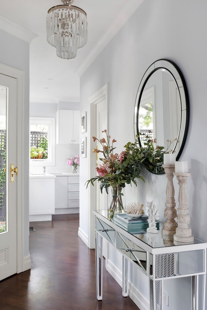 hamptons-entryway-with-mirror-console-and-round-mirror-pink-fake-plants-on-entry-table