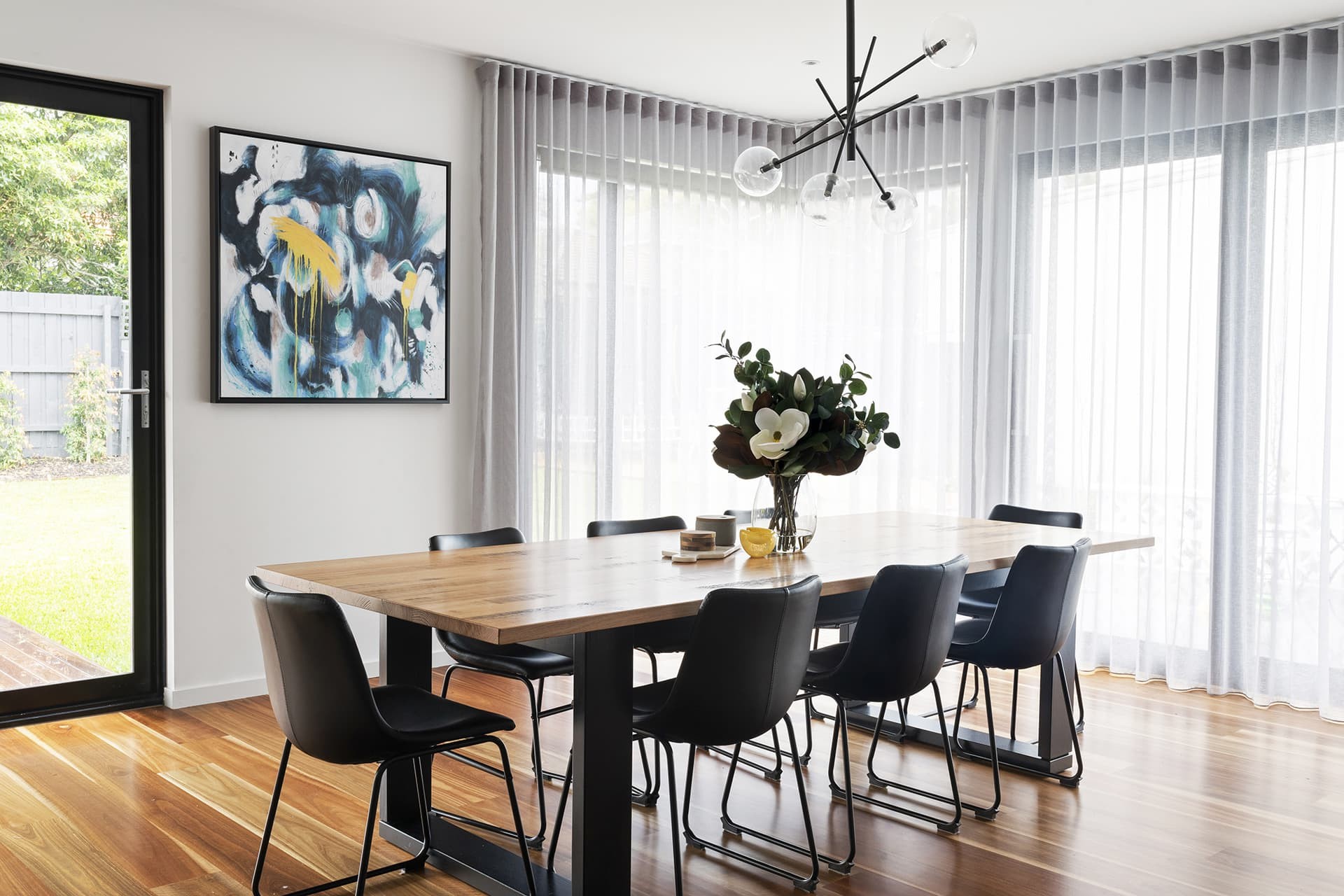 industrial dining table with australian natives and black leather dining chairs and sheer curtains