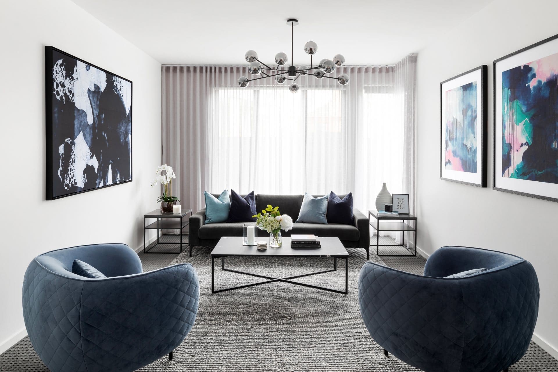 luxe formal living room with blue velvet armchairs and black marble coffee table grey sheer curtains