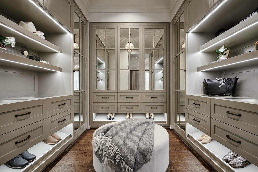 luxe walk in closet with mirror front doors and large round ottoman