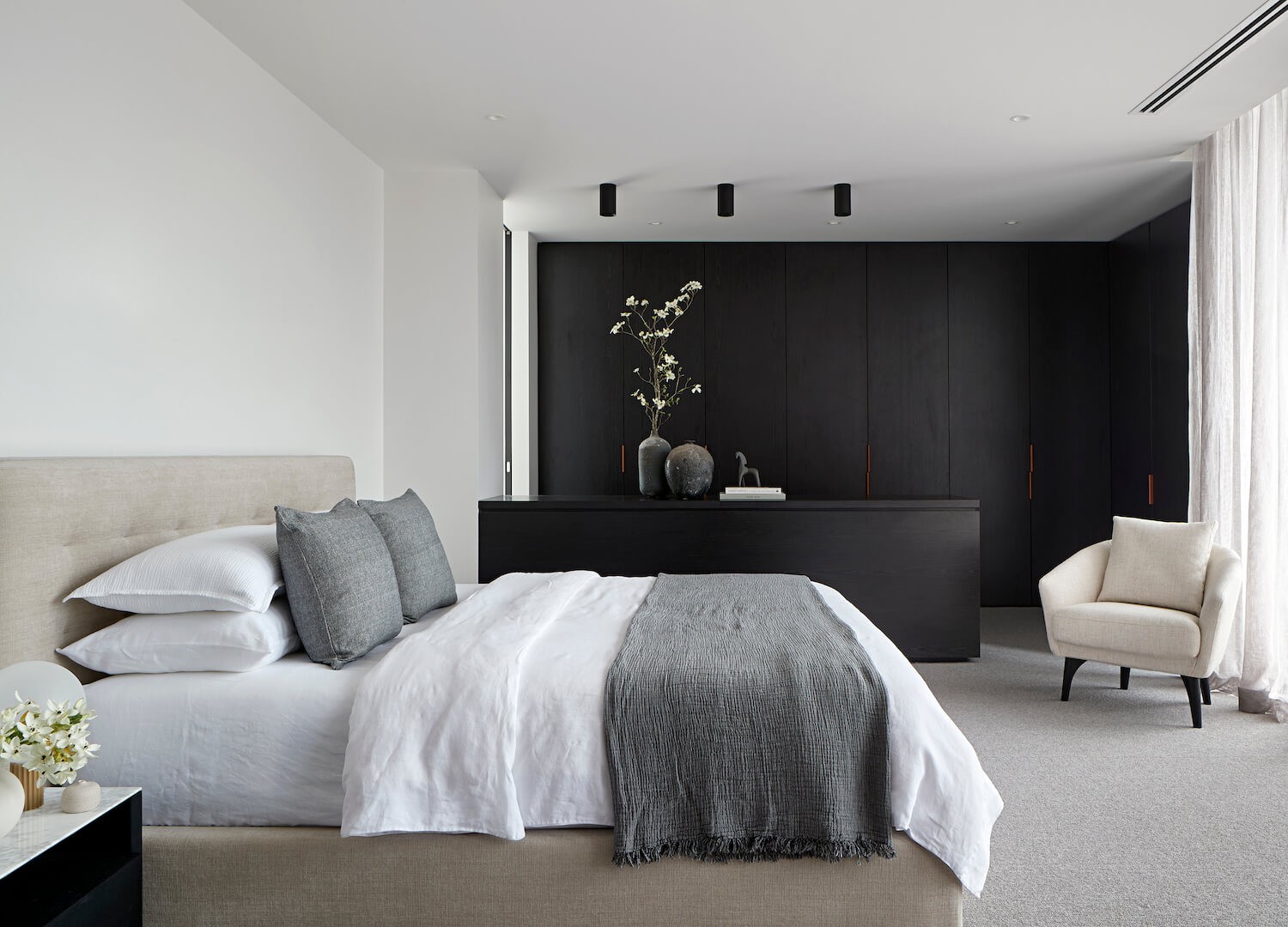 mans bedroom with white walls grey fabric bed and dark brown timber joinery