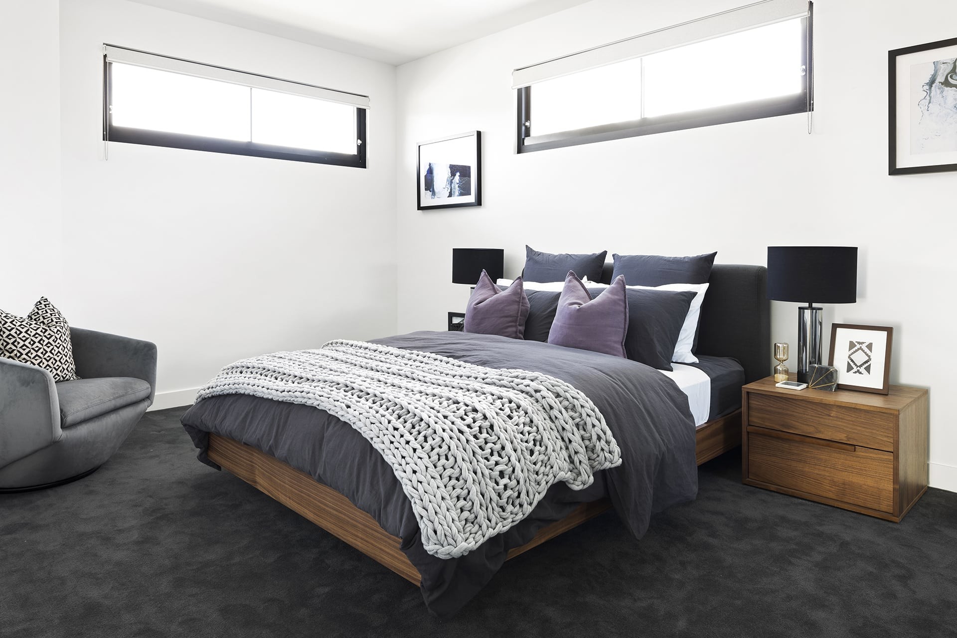 master bedroom with dark grey carpet brown timber bed and grey quilt cover set with purple cushions
