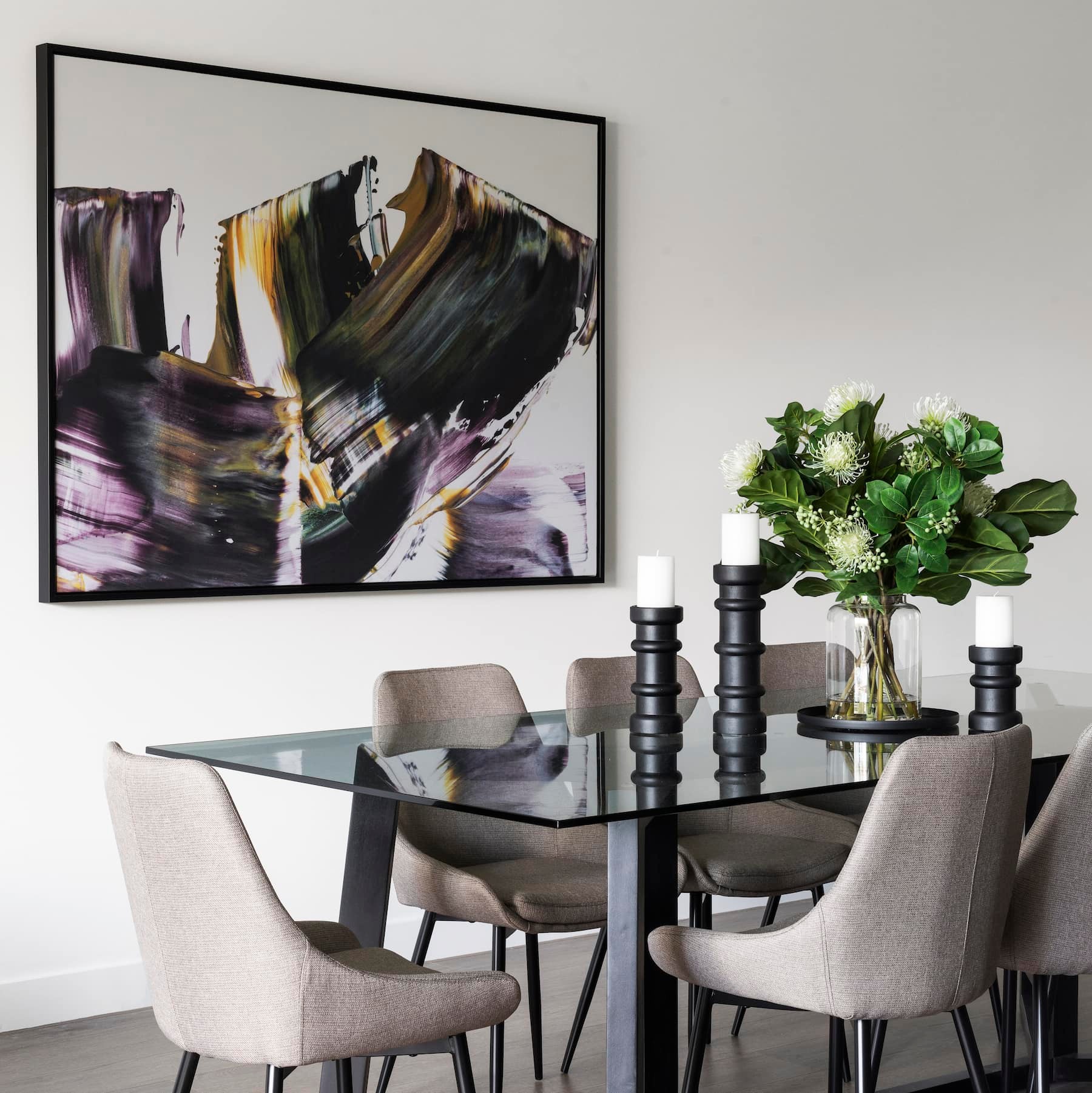 moody abstract art in dining room with glass top dining table and grey chairs