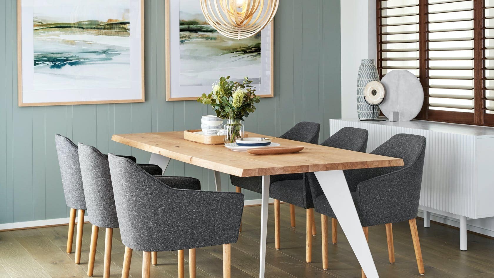 oak dining table with white metal legs in dining room with sage green feature wall