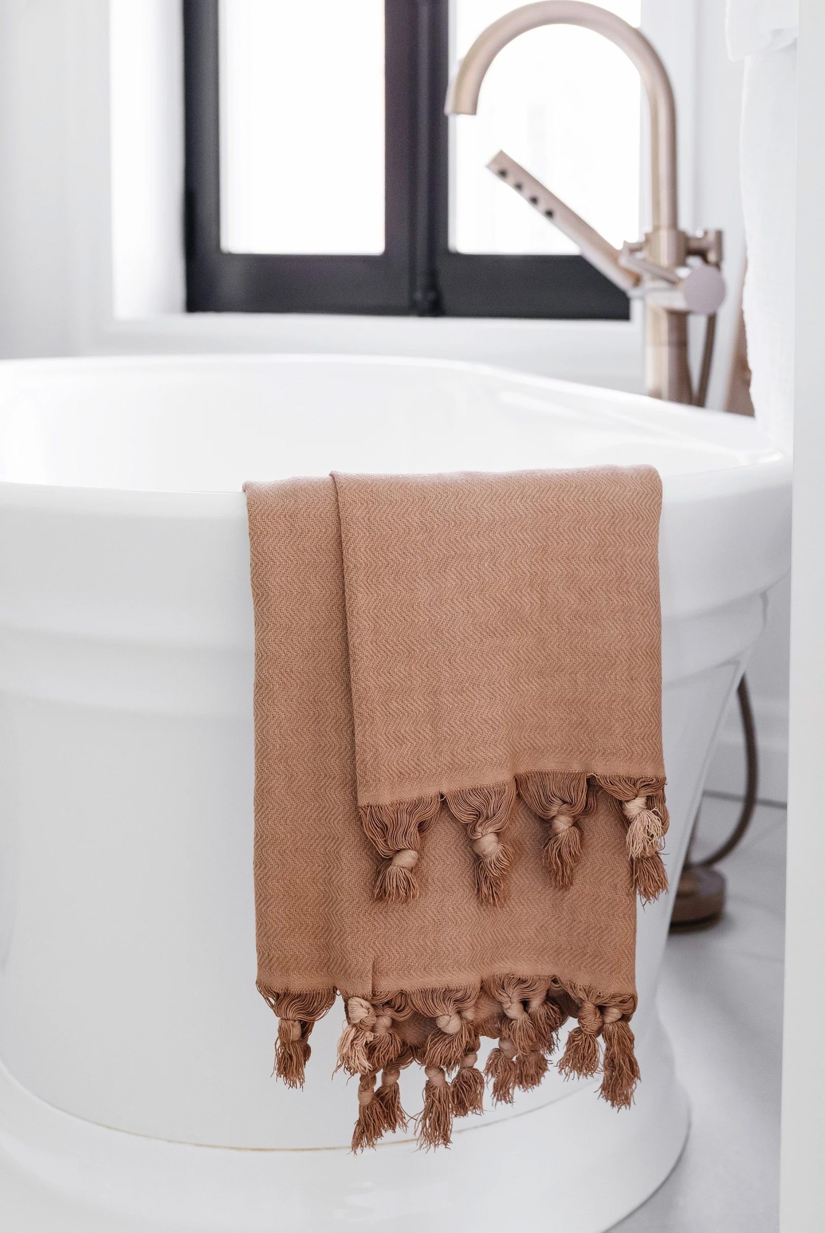 orange towel with pom poms on edge of white bath tub