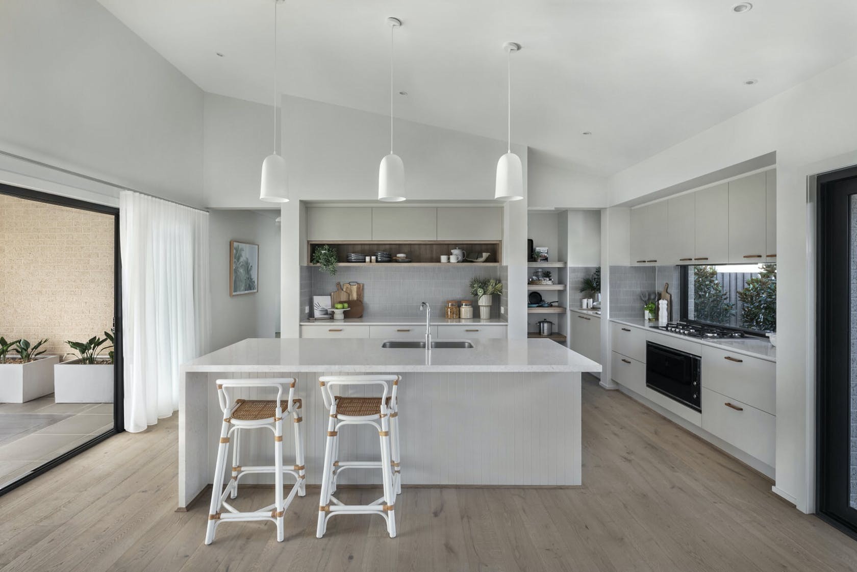three white pendant lights over island in coastal boho kitchen with timber styling