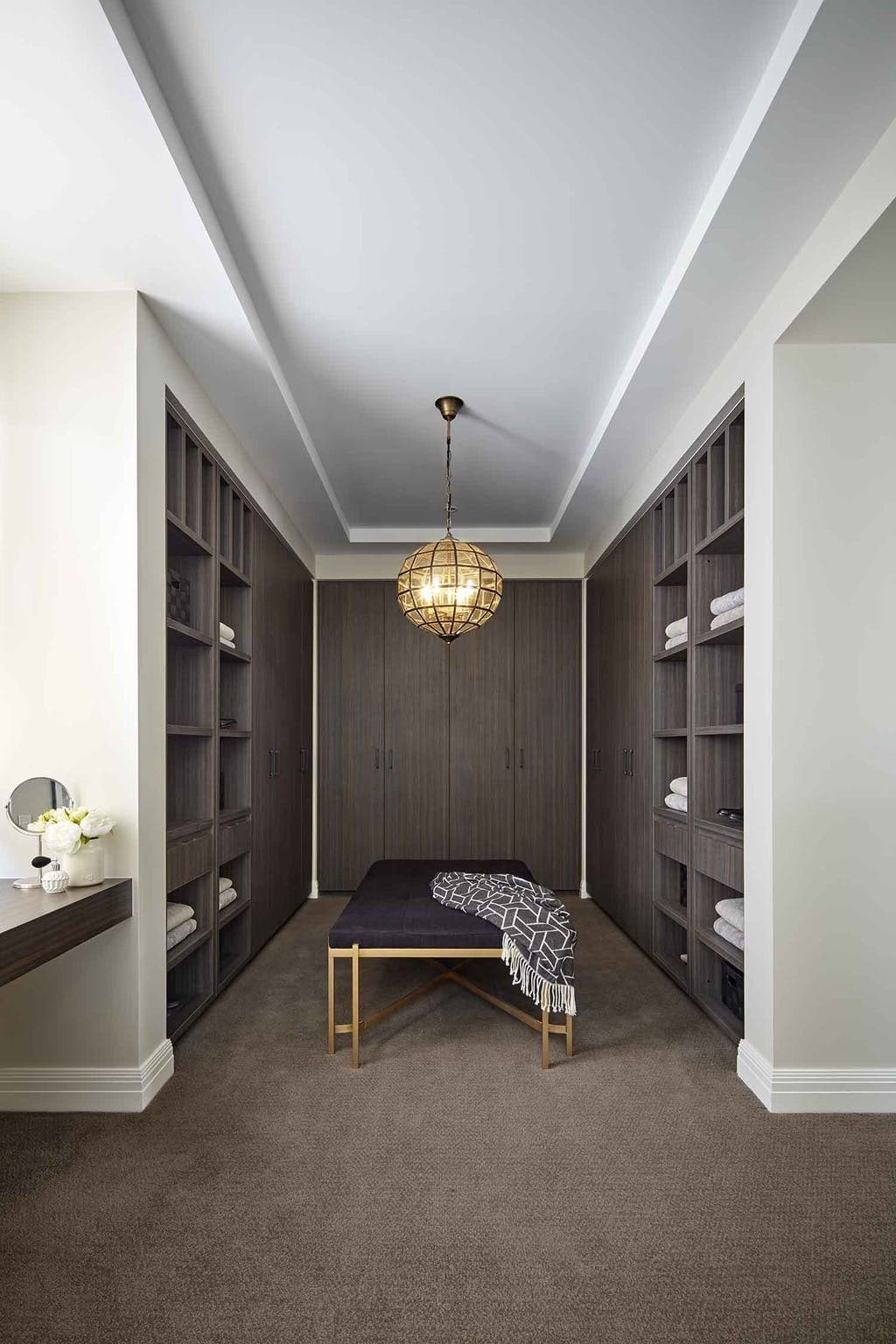 walk in closet with glass round feature pendant light and brass leg ottoman