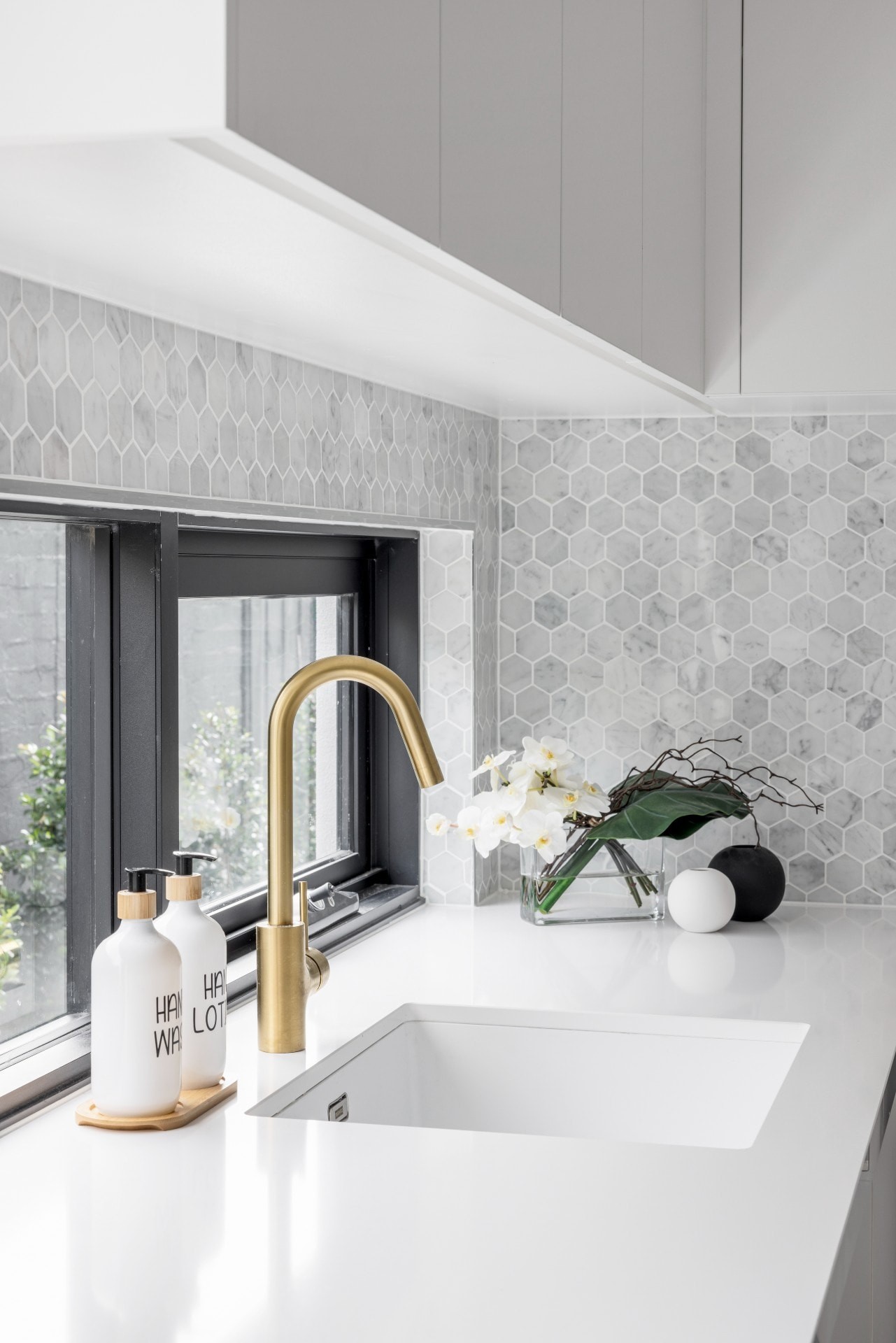 white and grey marble tiles in luxe laundry wih brass tapware and black window frame