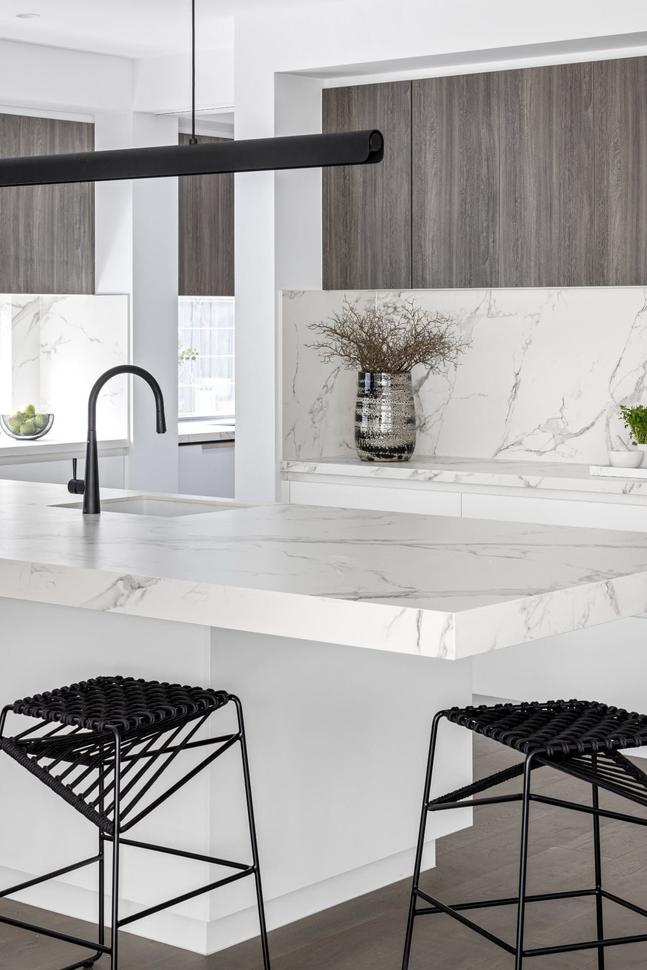 white marble kitchen with black stools tap and pendant light brown walnut upper cabinets