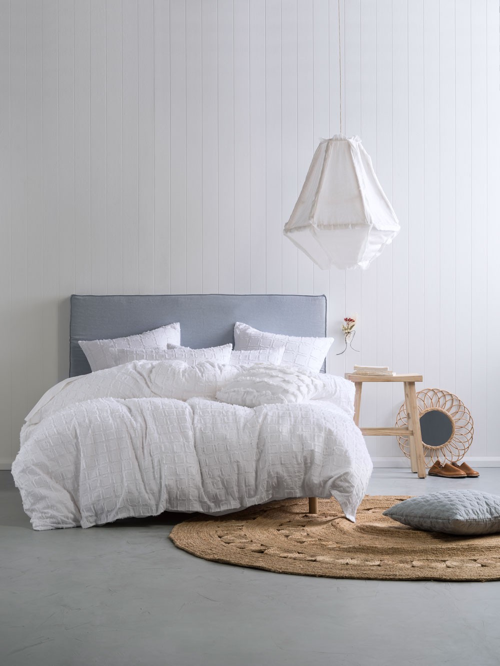 white timber panel bedroom with concrete floor and grey upholstered headboard and jute rug